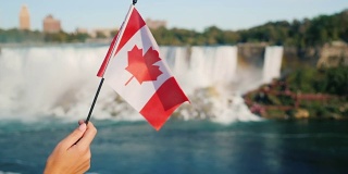 在尼亚加拉大瀑布的背景下，一只女性手举着加拿大国旗。在加拿大旅游