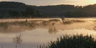 日出。早晨的风景。清晨的天空和它在水面上的倒影。夏天的早晨。河上有雾。远处渔夫在一只充气船上剪影