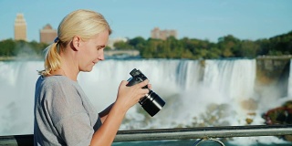 一个女人在看摄像机屏幕上的照片。以美丽的瀑布为背景。对假期的美好记忆