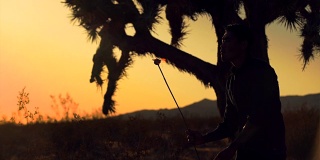日落时沙漠中吹火的人的慢镜头剪影