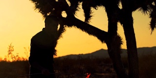 日落时沙漠中吹火的人的慢镜头侧面剪影
