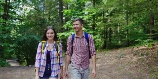 一对背着背包的年轻游客在树林里散步。温暖的夏天