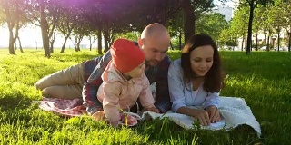 幸福的一家人躺在草地上，和孩子一起在公园里野餐，看一本书