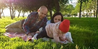 幸福的家庭躺在草地上，在野餐时读一本书，和孩子一起在公园里玩日落