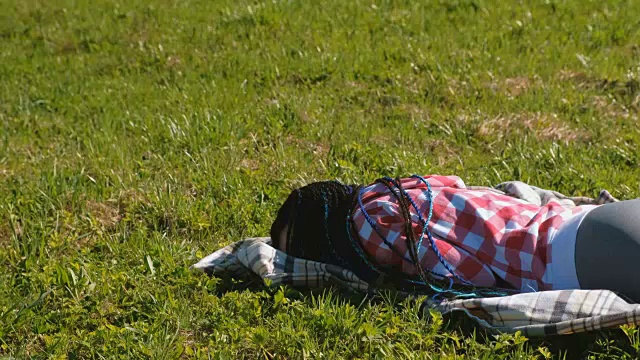梳着蓝色非洲辫的陌生女人睡在公园的草坪上。