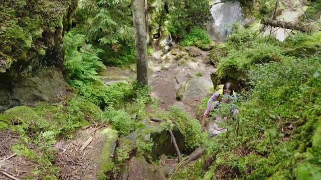 俯视图:一名男子帮助一名女子爬上陡峭的小路。在森林里徒步旅行