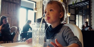 男孩坐在咖啡馆的桌子旁喝着橙汁杯