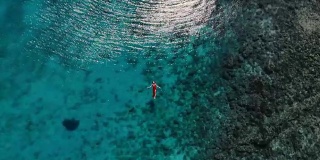 一个女人在热带海洋上漂浮和游泳的无人机视图