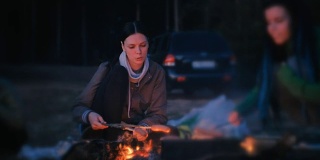 两个女人在火上煎香肠。晚上的家庭露营。