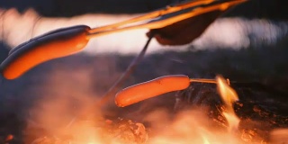 人们晚上在树林里用火煎香肠。特写香肠。