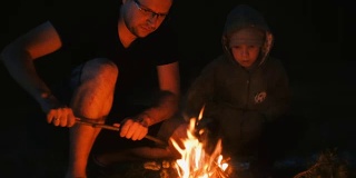 儿子和爸爸在森林里生火。家庭露营。