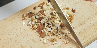 Chef's hands chopping mixed nuts on wooden cutting board