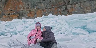 年轻的夫妇有乐趣在冬季散步的背景冰冻结的湖。情侣们坐在冰上，亲吻拥抱。快乐的年轻人在冰雪覆盖的冰面上漫步。蜜月。爱情故事。