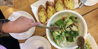 女人的手混合美味的超级食物凯撒沙拉配料与木汤匙在桌子上的餐厅大蒜面包和食物集。烹饪概念。前视图。