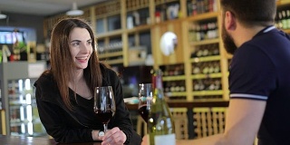 一个男人和一个女人正在用玻璃杯喝红酒，一个餐厅的内部，一个年轻的男人和一个女孩在一个餐厅的桌子上喝葡萄酒，背景是一个葡萄酒架子，一个男性嬉皮士