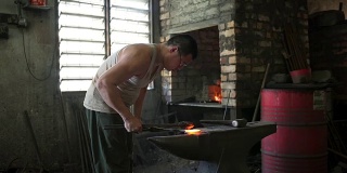 亚洲铁匠在他的车间里在铁砧上锻造热铁