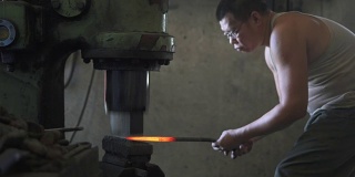 亚洲铁匠在他的车间里在铁砧上锻造热铁