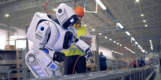 工厂的一名男性员工正在启动一个机器人，之后机器人就会启动并开始钻孔