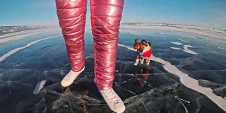 玩具小猎犬穿着滑稽的衣服和鞋子在裂缝里美丽的冰上玩球。妈妈和女儿穿着运动服和花样滑冰鞋。女孩们把玩具扔给狗。狗玩游戏。