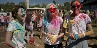 3个年轻的多民族女友在夏天的白天往胡里节上撒五颜六色的粉，欢笑着，友情概念，色彩概念