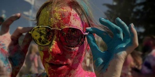年轻快乐的女孩穿着五颜六色的粉是戴着太阳镜在胡里节的白天在夏天，色彩概念