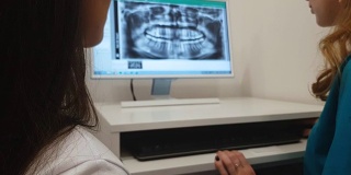 牙科医生在电脑上向病人展示牙齿x光图像，进行牙科诊断