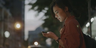 一名年轻女子站在街上，一边等出租车一边看手机。——股票视频