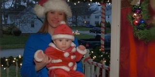 一位年轻的白人妈妈抱着一个婴儿，从前门走进一所装饰过圣诞节的房子