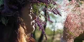 特写，美丽的女人与矢车菊花环在头上看起来盛开在粉红色的灌木在树林