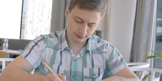一个年轻人在咖啡馆里用圆珠笔写字，慢镜头