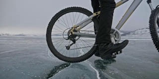 对轮胎的看法。180 fps射击。男人在冰上骑自行车。骑自行车的人从摄影机前面切过去了。碎冰飞进我们体内。自行车的轮胎上覆盖着特殊的尖钉。