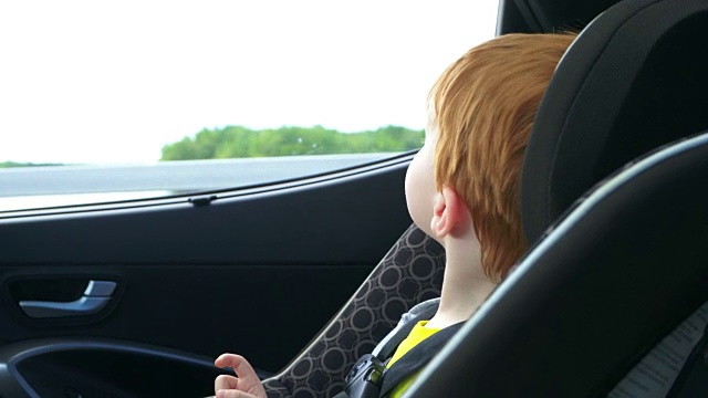快乐的蹒跚学步的男孩安全在汽车座位上的公路旅行