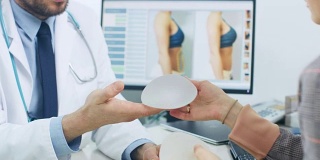 整形/整容外科医生为她的未来手术展示女性患者乳房植入样本。专业、著名的外科医生在体面的诊所工作。