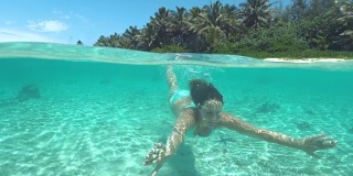 在一个完美的夏日里，快乐的年轻女子在碧绿的水中潜水