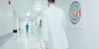 一个医生匆匆穿过医院走廊的背影。问候护士和同事。明亮的现代新诊所。