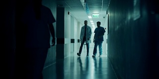 外科医生和医生匆忙穿过医院的黑暗走廊，一边谈论病人的健康。拥有专业人员的现代光明医院。