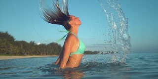近景:快乐的女人在假日玩她的头发在清澈的大海。
