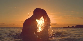 剪影:一名年轻女子把她的头发甩到后面，在夕阳下泼水。