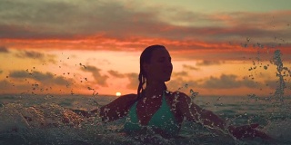 剪影:年轻女子微笑着在日落时分用手泼海水。
