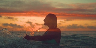 剪影:在一个阳光明媚的早晨，一个快乐的女人拖着她的手走过大海。