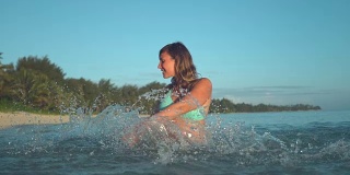 慢镜头:身着绿松石色衣服的快乐女子在透明的水中拖动手指。