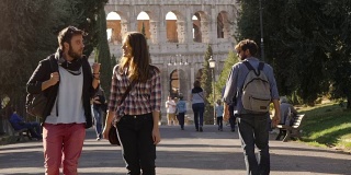 年轻幸福的夫妇走在公园路和有吸引力的年轻人瞥视女友gelousy与树木斗牛场在背景在罗马在日落可爱美丽的女孩与长发牵手慢动作