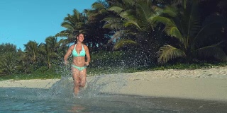 慢镜头:女子在浅海中奔跑，玻璃般的水滴在空中飞舞