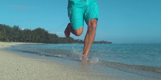 慢镜头:年轻的男子微笑着沿着壮观的沙滩奔跑。