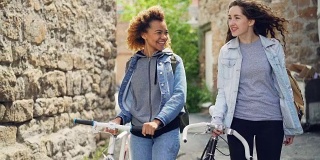 慢镜头，快乐的白人和非洲裔美国女孩，游客们笑着，骑着自行车沿着古老建筑的街道走着。旅游与人的观念。