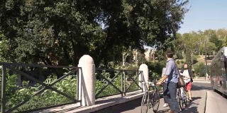 在阳光明媚的日子里，三个年轻的朋友骑着自行车在罗马市中心的罗马斗牛场周围的道路上散步