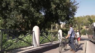 在阳光明媚的日子里，三个年轻的朋友骑着自行车在罗马市中心的罗马斗牛场周围的道路上散步视频素材模板下载