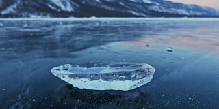 浮冰在冰面上旋转，映衬着令人惊叹的山景。缓慢的运动。镜头移到了冰的后面。冰在冰上旋转，有神奇的裂缝，非常漂亮。