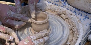 陶工大师的双手和陶工轮上的粘土花瓶