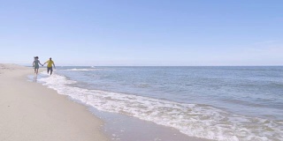 一对幸福的夫妇光着脚在海边散步，享受着自己的生活。白色沙滩。即将离任的沿海线。缓慢的运动。